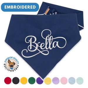May include: Navy blue dog bandana with white embroidered text "Bella" and a white border. The bandana is folded in half and has a white label with the text "Superior Quality Personalized". The image also shows a variety of colors for the bandana.