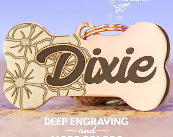 Puede incluir: Una placa de identificación para perro en forma de hueso de oro rosa con un diseño floral en un lado y el nombre "Dixie" grabado en el otro.