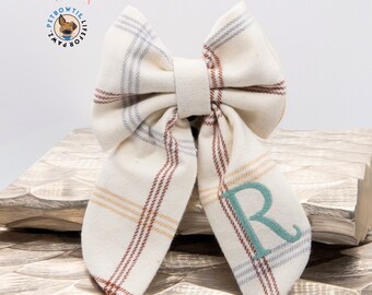 Op de afbeelding: Een witte geruite strik met een turquoise geborduurde letter "R" aan de ene kant. De strik is gemaakt door Pet Bow Tie Life for Paws.