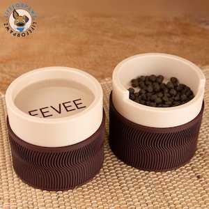 May include: Two brown and beige pet food containers with a wavy texture on the bottom. One container has the word "EEVEE" printed on the side. The other container has dry pet food inside.