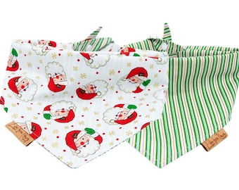 May include: Two reversible dog bandanas. One side features a white background with a repeating pattern of red and white Santa faces. The other side is green and white striped. Both bandanas have a brown tag with the text "Love You Much".