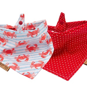May include: Two red and white bandana bibs with a snap closure. One bib has a white background with blue stripes and a red crab pattern. The other bib has a red background with white polka dots. Both bibs have a brown tag with the text "Life for Tiny."
