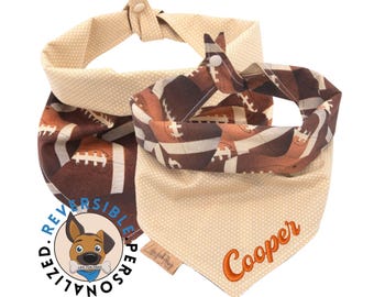 May include: A reversible dog bandana featuring a brown and white football design on one side and a beige polka dot pattern on the reverse. The bandana is personalised with the name "Cooper" in orange embroidery.