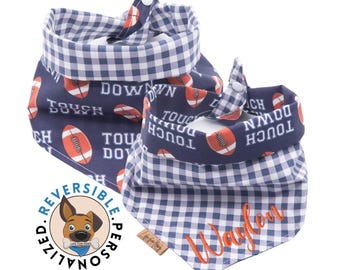 May include: Reversible dog bandana with a blue and white gingham pattern on one side and a navy blue pattern with footballs and the words "Touch Down" on the other side. The bandana is personalised with the name "Waylon" in orange thread.