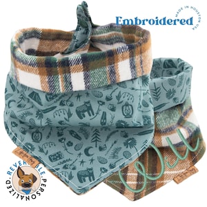 May include: Reversible dog bandana with a plaid pattern on one side and a blue and green pattern with camping icons on the other side. The bandana is embroidered with the word "Wild" in a light green color.