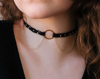 May include: A black choker necklace with a gold circle pendant and a delicate gold chain.