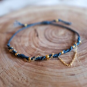 Könnte beinhalten: Ein dunkelblaues geflochtenes Armband mit goldenen Perlen und einer zarten goldenen Kette.