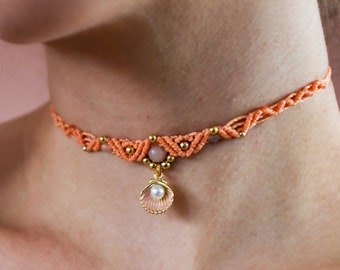 May include: A delicate orange and gold choker necklace with a small seashell pendant. The pendant features a pearl in the center.