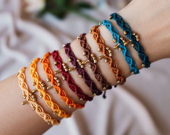 May include: A set of eight colorful braided bracelets with gold accents. Each bracelet features a unique color and a small gold charm.