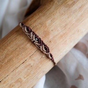 Peut inclure: Un bracelet d'amitié brun et beige avec un accent de perle argentée. Le bracelet est noué autour d'une bûche de bois.