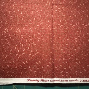 May include: Red fabric with a white floral pattern. The fabric has a label that reads "Hemming House by Brannock & Patek for moda www."