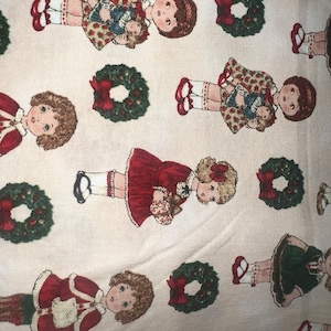 Puede incluir: Una tela blanca con un patrón repetido de coronas de Navidad rojas y verdes y muñecas que sostienen muñecas. Las muñecas llevan vestidos rojos, verdes y blancos.