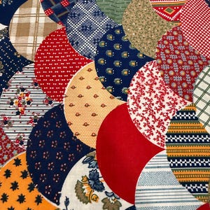 Puede incluir: Primer plano de un edredón colorido con una variedad de telas estampadas. El edredón presenta un diseño de semicírculos superpuestos en tonos de rojo, azul, naranja, verde y beige. Las telas incluyen estampados florales, lunares y patrones geométricos.