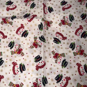 May include: A white fabric featuring a repeating pattern of snowmen wearing black top hats and red or green scarves. The snowmen are accented with small red dots and gold-colored snowflake shapes scattered across the entire surface of the material.