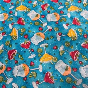 May include: A vibrant fabric featuring a repeating pattern of cocktail glasses in red, yellow, and clear, with orange and lime garnishes. Strawberries and lime wedges are scattered across a teal blue background, creating a summery, festive design.