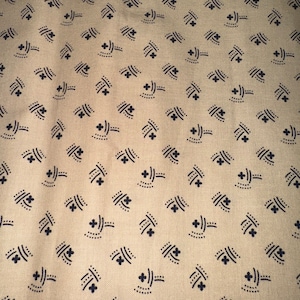 May include: A tan fabric featuring a repeating pattern of small, dark navy blue motifs. Each motif consists of a four-petaled flower shape accompanied by two curved lines and a series of tiny dots, arranged in a consistent, evenly spaced grid across the surface.