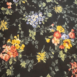 May include: Black fabric with a floral pattern featuring yellow, red, blue, and green flowers. The flowers are arranged in clusters and are surrounded by green leaves.