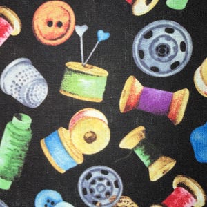 Peut inclure: Un tissu noir avec un motif répété d'articles de couture. Le motif comprend des bobines de fil de différentes couleurs, des boutons, des dés à coudre et des épingles. Les bobines ont du fil jaune, rouge, vert, bleu et violet.