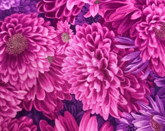 Op de afbeelding: Close-up van een stof met een levendig bloemenpatroon. Het ontwerp toont grote, roze en paarse chrysantenbloemen met gedetailleerde bloemblaadjes en groene centra. De stof is 100% katoen.