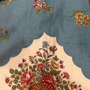 Pode incluir: Tecido floral com fundo azul claro e um padrão repetido de pequenas flores. Um grande arranjo floral decorativo em uma cesta é apresentado em uma borda creme com vieiras.