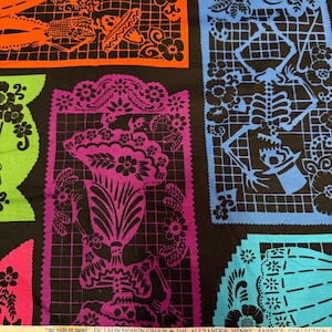 Może przedstawiać: Czarna tkanina z kolorowymi ilustracjami szkieletów w stylu papel picado w kolorach pomarańczowym, niebieskim, zielonym, fioletowym i turkusowym. Na krawędzi znajduje się napis "mi vida en papel" DE LEON DESIGN GROUP THE ALEXANDER HENRY FABRICS COLLECTION.