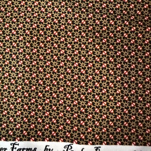 May include: A black fabric featuring a repeating geometric pattern of small gold star-like shapes and tiny red and white oval accents. The white selvage edge displays the printed text "Farms by Paula Barnes" in a black serif font.