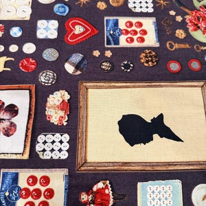 May include: A dark purple fabric covered with various vintage-style embellishments. The design includes buttons, keys, framed silhouettes, and floral accents in red, white, and gold. The overall aesthetic is a collage of antique and craft elements.