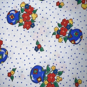 May include: White fabric with a repeating pattern of blue vases filled with red, yellow, and blue flowers. The background has a polka dot design of small blue dots. The fabric has a vintage, floral theme.