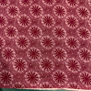 May include: Burgundy fabric with a repeating floral pattern. The design features dark red stylized flowers with white dot accents, set against a textured background. The fabric is measured in inches.