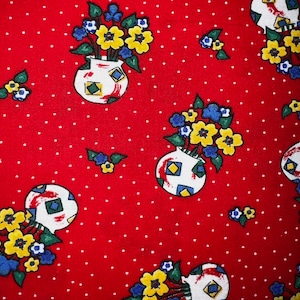 May include: Red fabric with a white polka dot pattern and a repeating pattern of yellow and blue flowers in white pots with geometric designs.