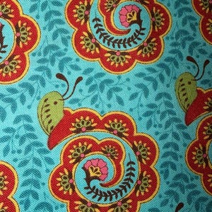 May include: Close-up of a teal fabric with a repeating pattern of red and yellow floral designs. Each design has a central spiral and is accompanied by a green butterfly. The background features small teal leaf shapes.