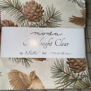 Puede incluir: Una tela blanca con un estampado de piñas y pájaros marrones y verdes. La tela está etiquetada "moda Midnight Clear by 3 Sisters for moda".