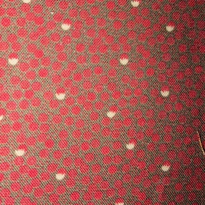 May include: Close-up of a fabric with a repeating pattern of red circles with white half-circles on a dark gray background. The fabric has a textured appearance.
