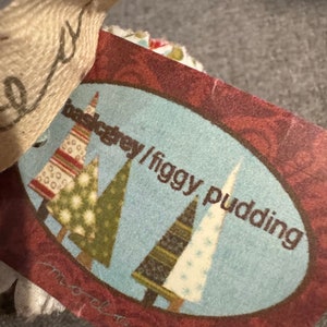 Może przedstawiać: Czerwono-biała metka z niebieskim tłem i wzorem trzech choinek. Na metce widnieje napis "backgrey/figgy pudding".
