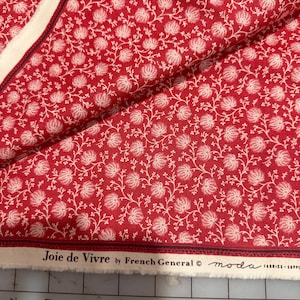 May include: Red fabric with a white floral pattern. The fabric features a repeating design of stylized flowers and vines. The selvedge edge has the text "Joie de Vivre by French General" and the Moda Fabrics logo.