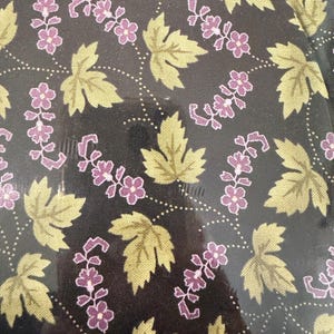 Peut inclure: Gros plan sur un tissu avec un motif répété de feuilles et de fleurs stylisées. Les feuilles sont d'un jaune-vert sourd et les fleurs d'un violet profond. Le fond est de couleur charbon de bois foncé, avec des lignes pointillées reliant les éléments floraux.