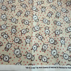 Może przedstawiać: Kremowa tkanina z wzorem białych budzików i małych różowych kropek. Zegary mają czarne kontury. Na tkaninie wydrukowano tekst "All in A Day" autorstwa Anni Downs.