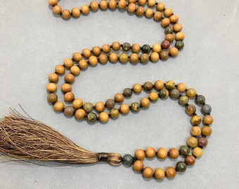 May include: A brown wooden mala bead necklace with a brown tassel. The beads are made of wood and have a natural, earthy look. The tassel is made of a soft, silky material.