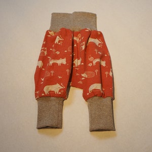 May include: Red and beige baby trousers with a white animal print. The trousers have a cuffed leg and a waistband.
