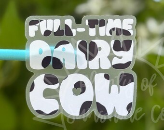 May include: A clear sticker with the words "FULL-TIME DAIRY COW" in white and blue bubble letters. The word "DAIRY" has black cow spots. The sticker is held by a light blue stick against a blurred green background.