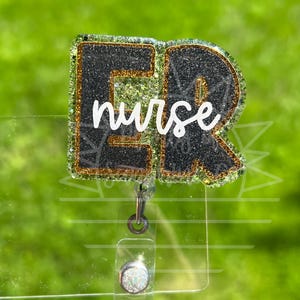 Peut inclure: Un porte-badge avec les lettres "ER" en paillettes noires avec une bordure en paillettes dorées, et le mot "nurse" en écriture blanche. Le porte-badge est fixé à un support en plastique transparent avec un clip argenté et un bouton décoratif.