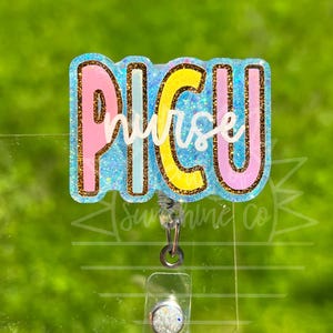 Peut inclure: Un porte-badge avec le texte "PICU Nurse" en rose, jaune et paillettes bleues. Le porte-badge a un support en plastique transparent et un clip argenté.