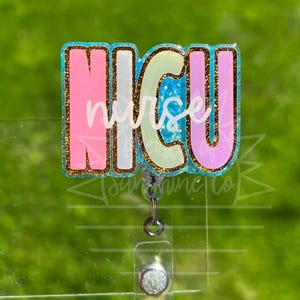 Peut inclure: Un porte-badge avec le texte "NICU nurse" dans un design coloré. Les lettres sont soulignées de paillettes et remplies de rose, de blanc et de vert. Le porte-badge a une sangle en plastique transparent et un clip argenté.