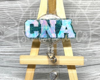 May include: A teal blue and iridescent glitter badge reel with the word "CNA" in white letters. The reel is attached to a clear plastic retractable cord and a silver clip.
