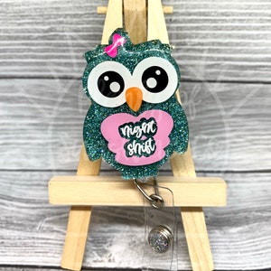 May include: Teal glitter owl with a pink bow and a pink heart that says "night shift" on it. The owl is attached to a clear retractable badge holder with a silver clip.