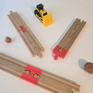 May include: Wooden toy train tracks with red connectors and a yellow and black toy bulldozer. The tracks are made of light brown wood. The bulldozer has a yellow scoop and black wheels.