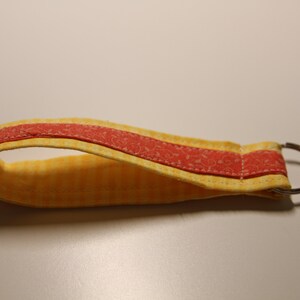 May include: A yellow and red fabric key chain with a silver metal ring.