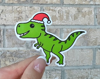 May include: A green dinosaur wearing a red Santa hat. The dinosaur is standing on its hind legs with its tail curled up behind it.