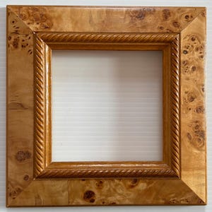 May include: A square wooden picture frame with a rope-like design around the inner edge. The frame is made of light brown wood with a burl wood pattern.