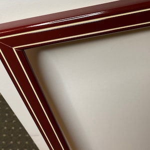 May include: A red picture frame with a white double border. The frame is made of wood and has a glossy finish.